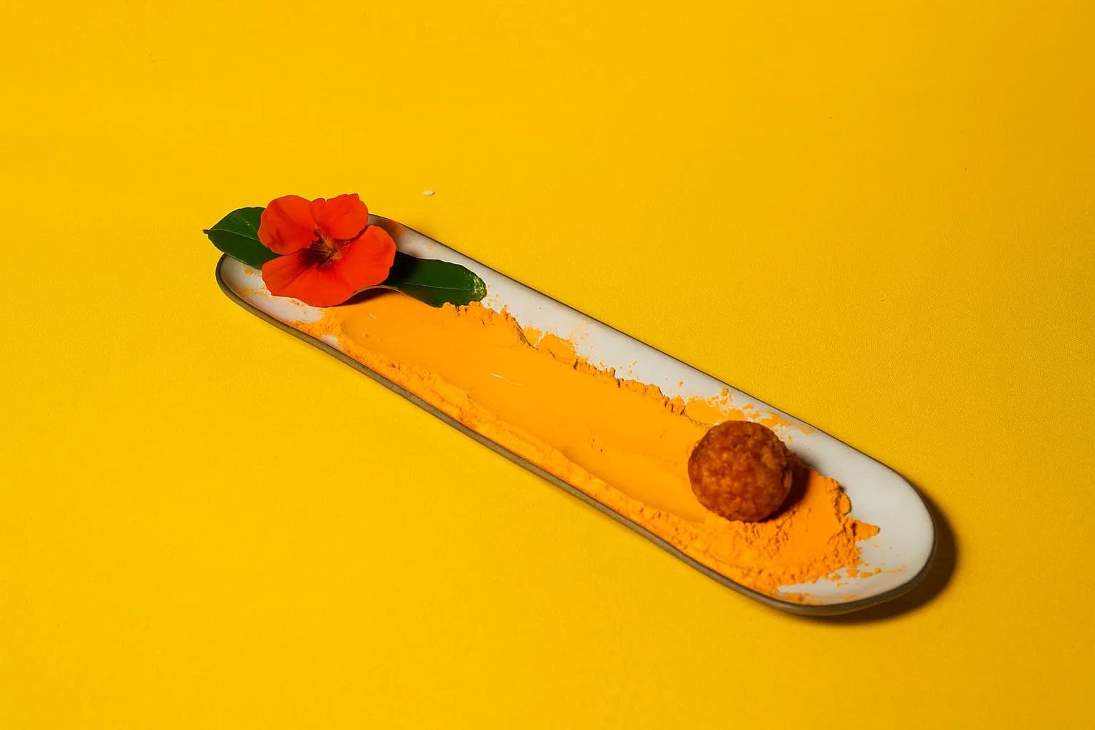 Croqueta sobre crema anaranjada en plato alargado