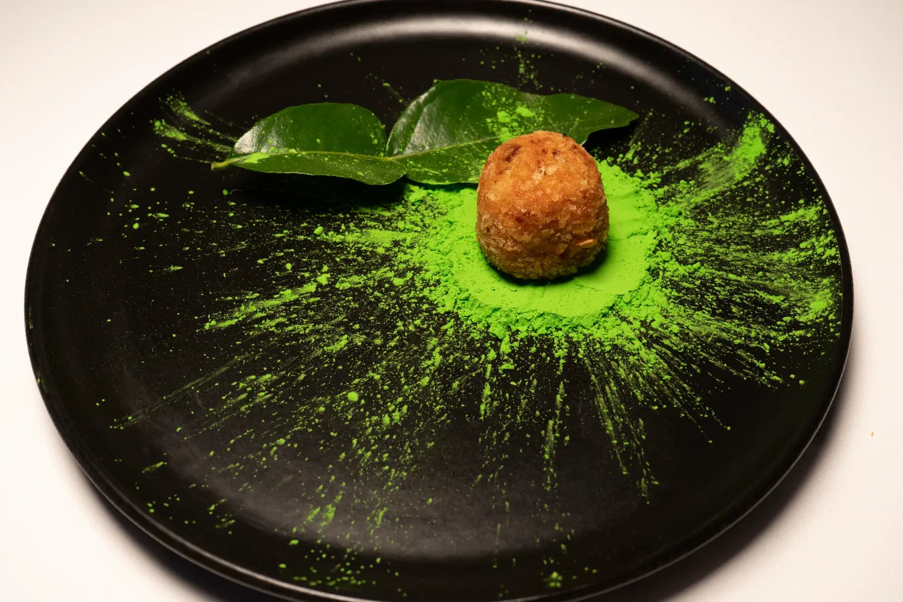Croqueta sobre plato negro con polvo verde de matcha