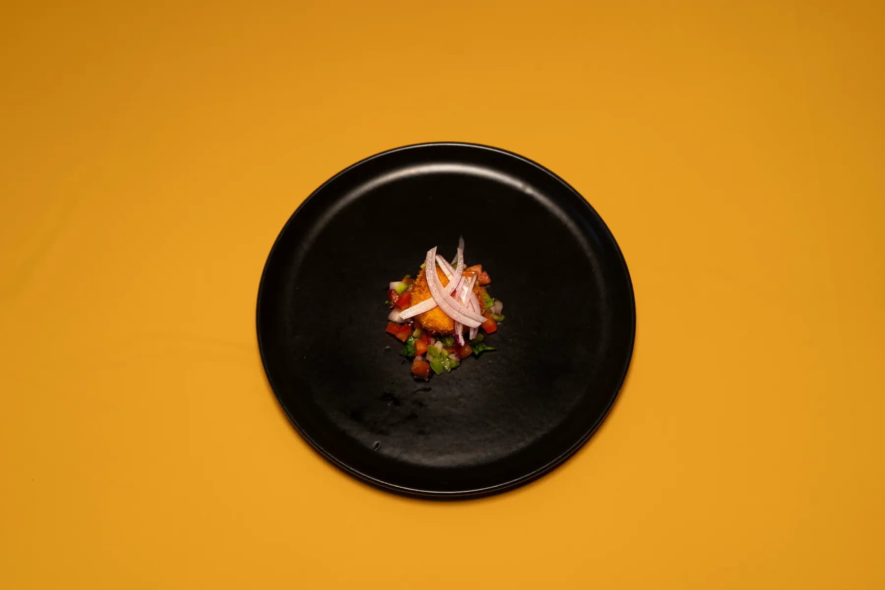 Croqueta artesana de Crocant con pico de gallo, en plato negro sobre fondo amarillo