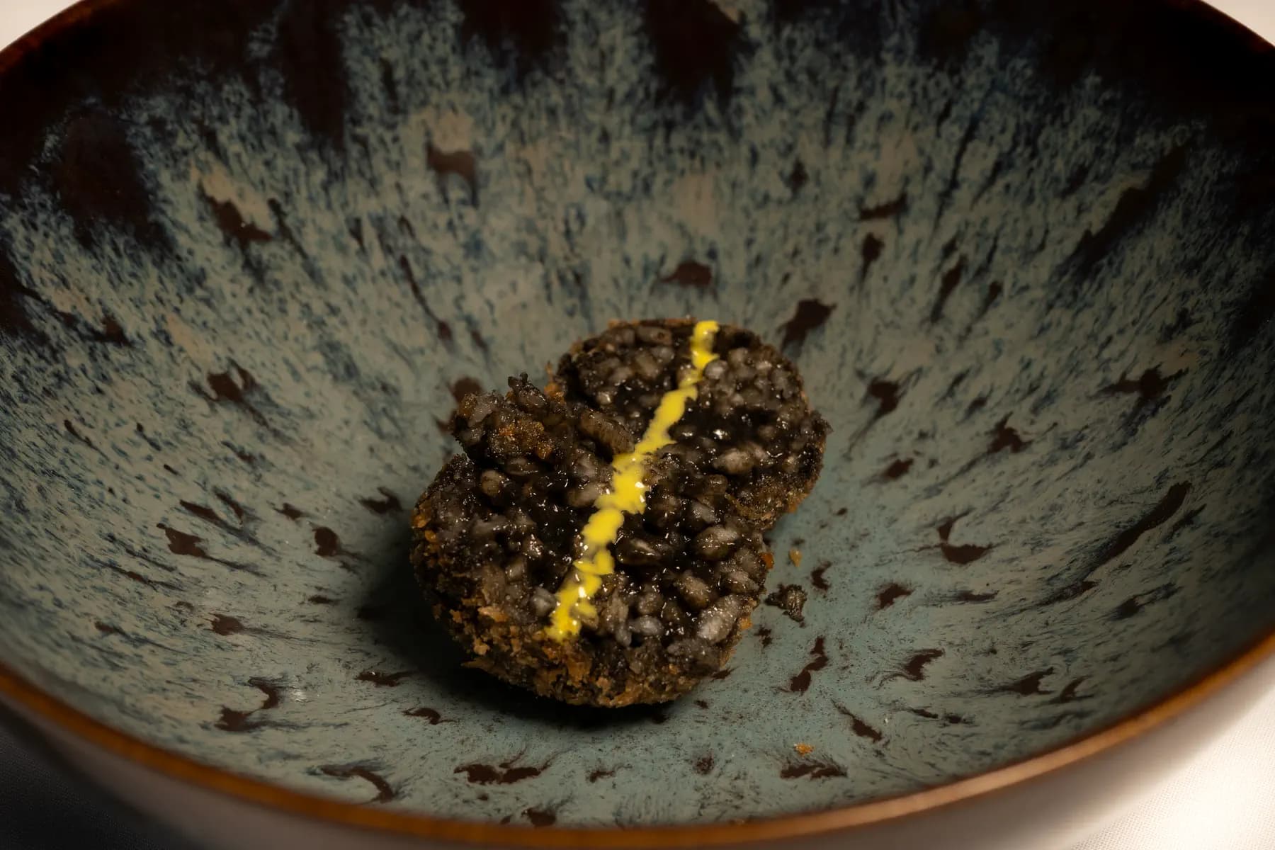 Croqueta de tinta con un hilo de alioli, en detalle